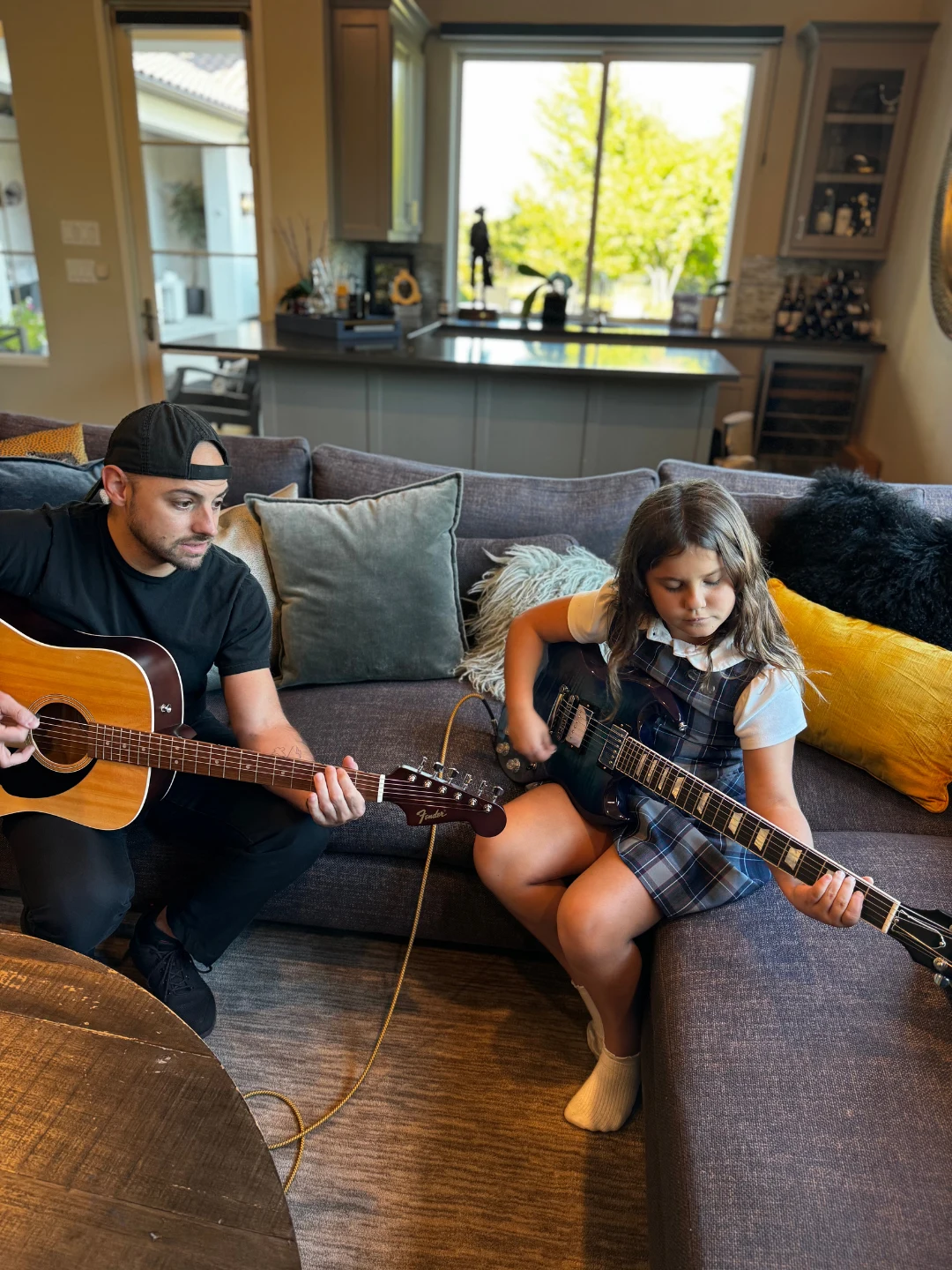 Mr. Garrett playing acoustic guitar alongside a student practicing electric guitar at home